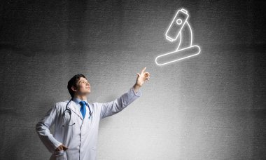 Arka planda gri koyu duvara ayakta iken beyaz üniforma havada parlayan mikroskop simgesi ile interracting genç erkek doktor.