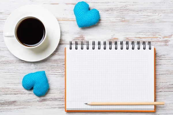 Coffee cup notepad pencil and two hearts on wooden surface