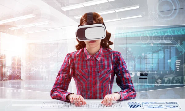 Educational process with help of VR headset. Cheerful young woman in checkered shirt using digital media interface while sitting indoors of office building.