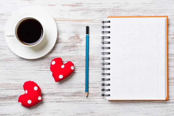 Coffee cup notepad pencil and two red hearts on wooden surface