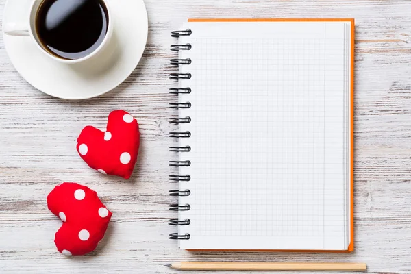 Coffee cup notepad pencil and two red hearts on wooden surface