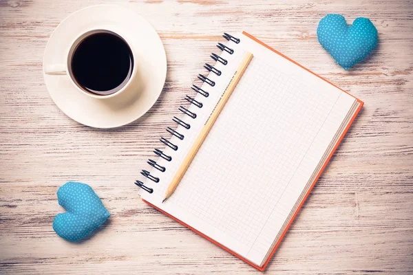 Coffee cup notepad pencil and two hearts on wooden surface