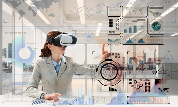 Horizontal shot of young successful business woman sitting inside office and using virtual reality headset with digital media interface