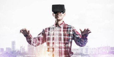 Sanal gerçeklik kulaklığı olan genç bir adam ya da şehrin arka planında 3 boyutlu gözlüklü.