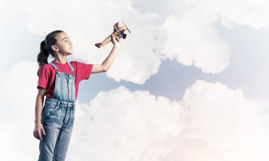 Elinde retro uçak modeliyle tulumlu şirin bir kız çocuğu.