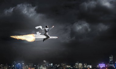 Arka plan üzerinde gece cityscape ve mavi gökyüzü ile roket üzerinde uçan takım elbiseli genç işadamı kavramsal görüntü.