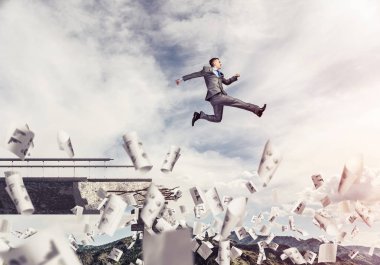İşadamı, sorunların üstesinden gelmenin sembolü olarak uçan kağıtlar arasında köprüdeki boşluktan atlıyor. Arka planda güneş ışığı ve doğa manzaralı gökyüzü. 3B görüntüleme.