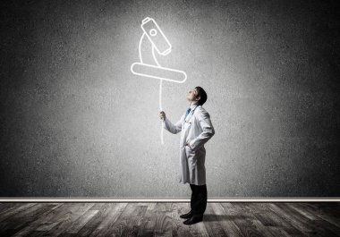 Arka planda gri duvara ayakta iken beyaz üniforma havada parlayan mikroskop simgesi ile interracting genç erkek doktorun kavramsal görüntü.