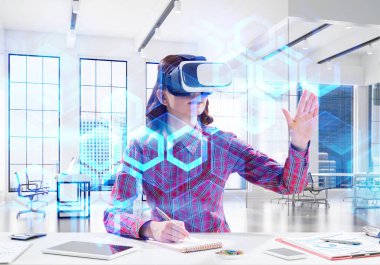 Parlak ofis binası içinde otururken sanal gerçeklik kulaklık ve medya arayüzü ile interracting kullanarak damalı gömlek genç ve güzel kadın kavramsal görüntü.