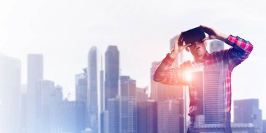Sanal gerçeklik kulaklığı olan genç bir adam ya da şehrin arka planında 3 boyutlu gözlüklü.