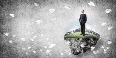 Yeşil yüzen adada beton zemine karşı duran kendine güvenen zarif iş adamı.