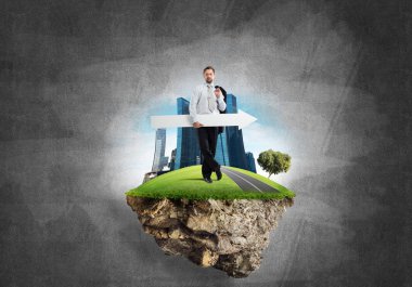 Takım elbiseli genç bir işadamı uçan adada elinde kocaman beyaz bir afişle dikiliyor. Arkasında gri, siyah bir duvar var.