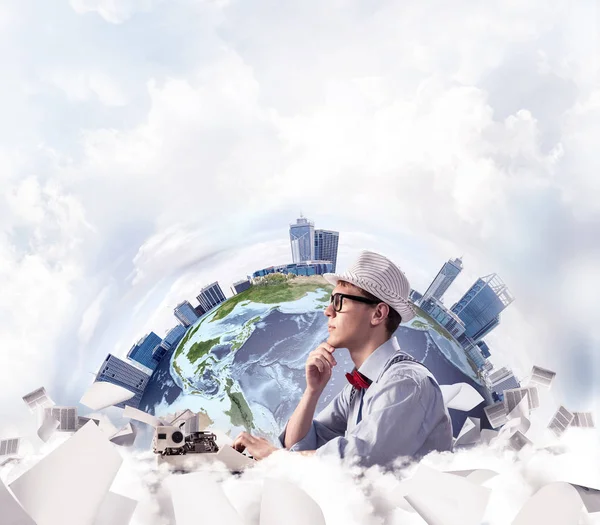 Side view of thoughtful man writer in hat and bow-tie looking away and touching chin while using typing machine with flying papers and Earth globe among cloudy skyscape on background. Elements of this image furnished by NASA