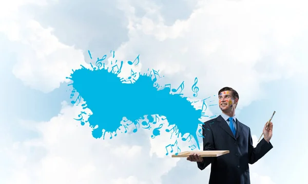 曇り空の景色の背景に対して青い色音楽スプラッシュと立っている黒い服を着て明るく 若いビジネスマンの水平ショット — ストック写真