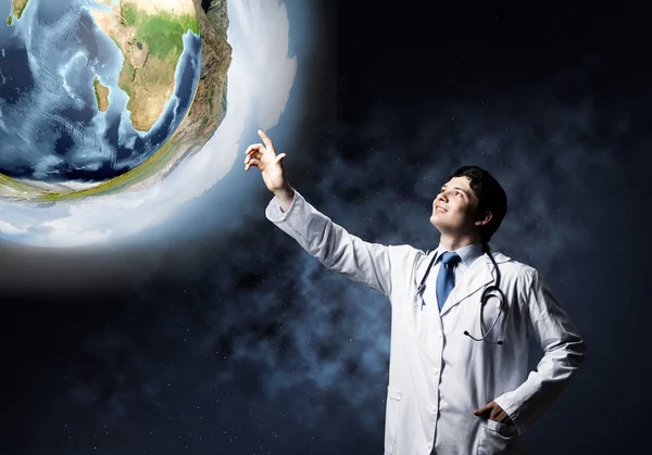 Conceptual image of confident young doctor in white medical uniform standing in dark outer space and looking at Earth globe on background. Elements of this image are furnished by NASA