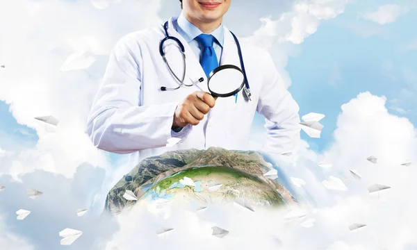 白い医療制服ルーペを通して見ると背景に曇り空の景色と 地球世界を勉強の若い医者のクローズ アップ 医療業界の概念 Nasa から提供されたこのイメージの要素 — ストック写真