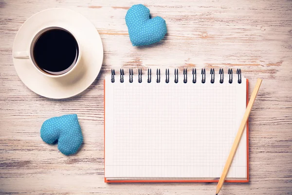 Kahve fincanı not defteri kalem ve ahşap yüzeyde iki kalp