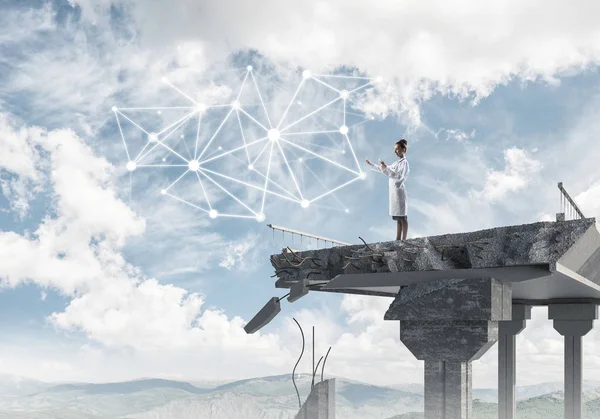 Kırık köprü sonunda akıllı telefon kullanarak beyaz üniforma ve sosyal medya ağ yapısı ile interracting emin kadın doktor. Tıbbi endüstri konsepti. Arka planda peyzaj görünümü