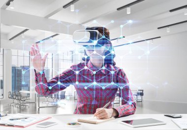 Parlak ofis binası içinde otururken sanal gerçeklik kulaklık ve medya arayüzü ile interracting kullanarak damalı gömlek genç ve güzel kadın kavramsal görüntü.