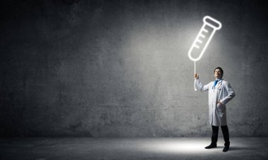 Arka planda koyu gri duvara karşı parlayan şişe sembolü whie ayakta beyaz Tıbbi üniforma genç güvenilir doktor yatay çekim.