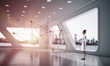 Beyaz hastane binası içinde ayakta iken ağ yapısı okuyan beyaz tıbbi elbise genç kadın doktor. Medikal Sanayi konsepti
