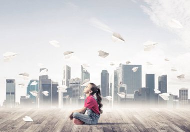 Ahşap zemin ve etrafında uçan kağıt uçaklar üzerinde oturan sevimli kız