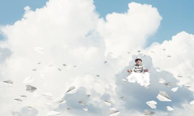 Küçük çocuk gözlerini kapalı tutuyor ve odaklanmış görünüyor. Arka planda bulutlu bir gökyüzü ile havada uçan kağıt uçaklar arasında meditasyon yapıyor..