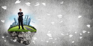 Yeşil yüzen adada beton zemine karşı duran kendine güvenen zarif iş adamı.