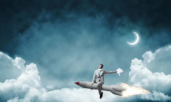 蓝夜影像 中的年轻商人的概念形象与云和月亮的背景下的火箭飞行 — 图库照片