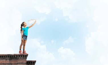 Binanın tepesinde kağıt uçakla oynayan sevimli, mutlu bir kız.