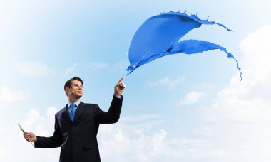 Arka planda bulutlu gökyüzü mavi renkli sıçrama ile siyah takım elbise ayakta neşeli ve genç işadamı yatay çekim.