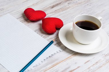 Kahve fincanı not defteri kalem ve ahşap yüzeyde iki kırmızı kalp