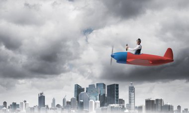 Havacı şapkalı işadamı ve fırtınada pervane uçağı süren gözlükler. Küçük bir uçakta pilotun yan görünümü. Dramatik karanlık bulutlu gökyüzü ile Megalopolis panorama. Karma medya iş kavramı.