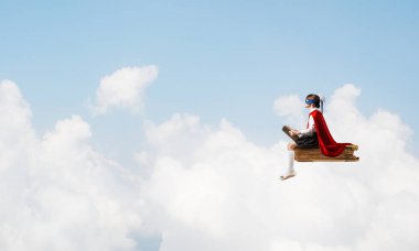 Maskeli ve pelerinli küçük çocuk gökyüzünde yüzüyor ve kitap okuyor.