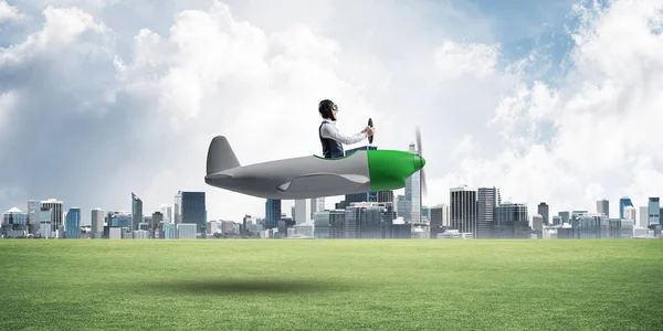 商人在飞行员帽子和护目镜驾驶螺旋桨飞机 市中心有高楼大厦 飞机上的人低空飞行 现代大都市全景与绿草和多云的天空 — 图库照片