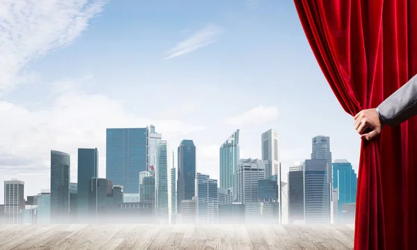 Cidade de negócios em nevoeiro cinza atrás de cortina vermelha e mão segurando-o — Fotografia de Stock