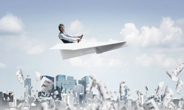 Screaming pilot sitting in paper plane and holding steering wheel. Aviator driving paper plane in blue sky above falling paper sheets with infographics. Cityscape with skyscrapers and office buildings