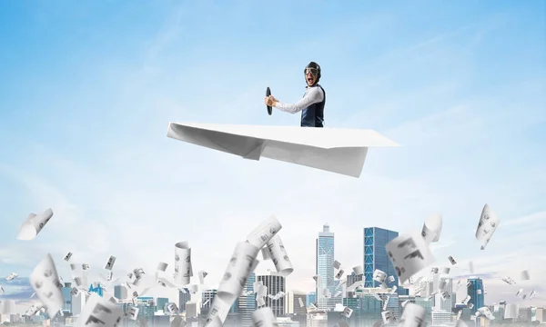Screaming pilot sitting in paper plane and holding steering wheel. Aviator driving paper plane in blue sky above falling paper sheets with infographics. Cityscape with skyscrapers and office buildings