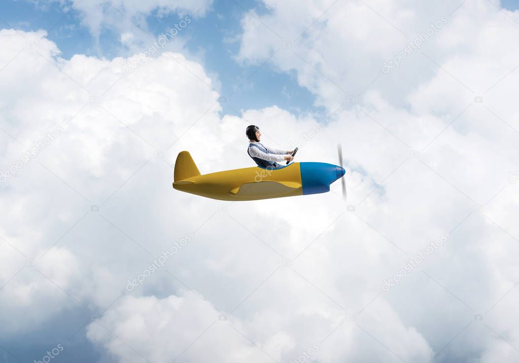 Happy pilot driving small propeller plane on background of blue sky with clouds. Traveling around the world by airplane. Funny man flying in small airplane. Cloudscape background with fluffy clouds.