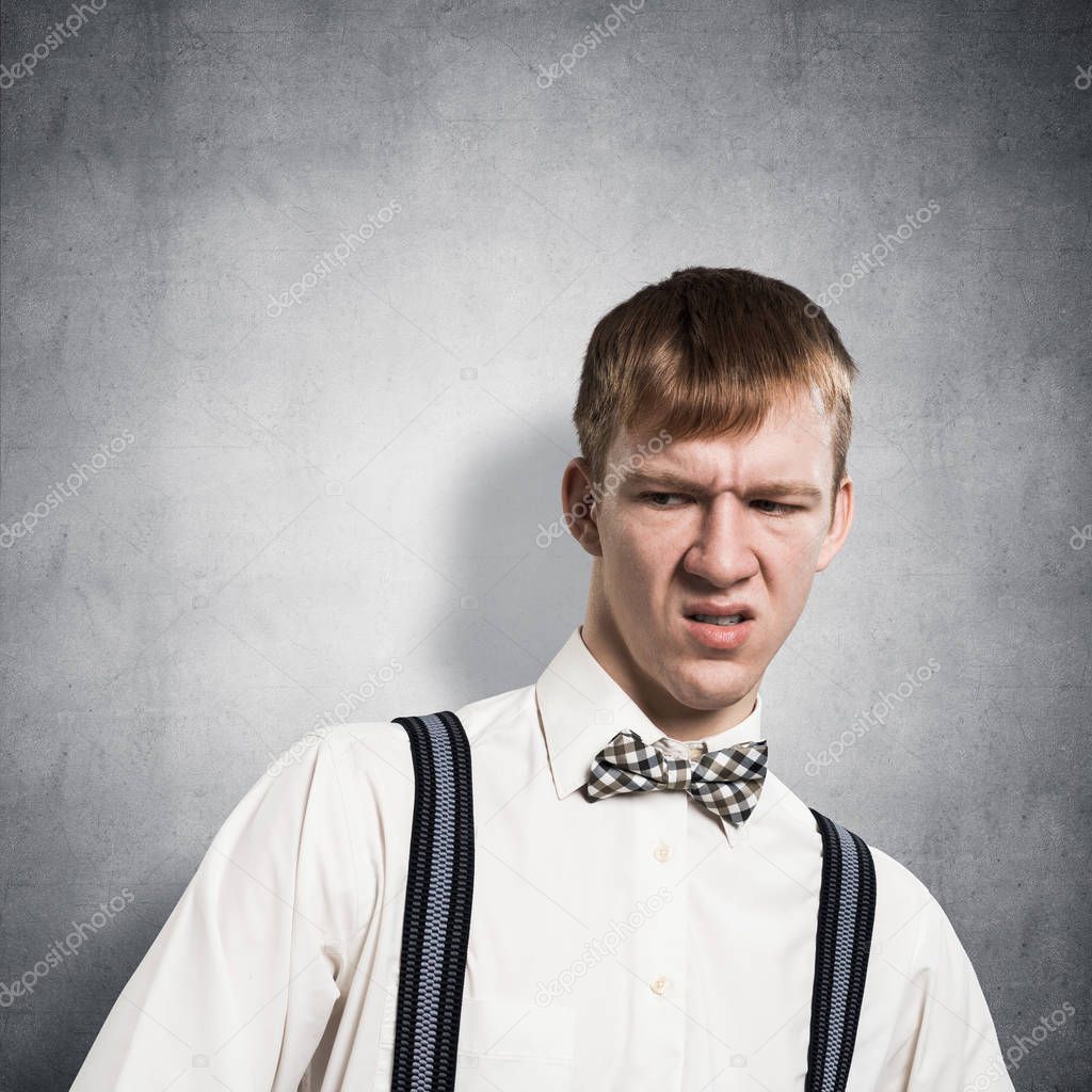 Ugh, how disgusting. Displeased redhead hipster. Emotional boy has dissatisfied facial expression as sees something abominable or detestable. Portrait of guy wears white shirt, bow tie and suspenders