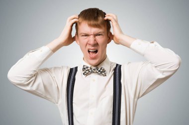 Stresli hippi öfkeyle bağırıyor ve ellerini başının üstünde tutuyor. Duygusal kızıl oğlanın yüzünde tahriş olmuş bir ifade var. Adamın portresi gri arka planda beyaz gömlek, papyon ve pantolon askısı takıyor.