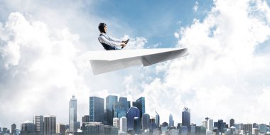 Kağıt uçakta oturan pilot ile iş motivasyonu kavramı. Havacı şapkalı komik adam ve şehrin üzerinde kağıt uçak süren gözlükler. Rüyada gökyüzünde uçmak. Yüksek binalarile modern megapolis.