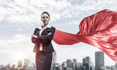 Young confident businesswoman wearing red cape against modern city background clipart