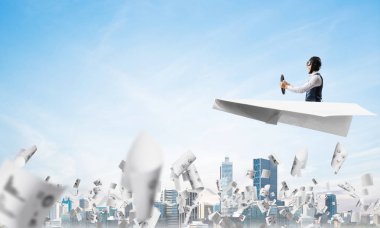 Havacı bulutlu mavi gökyüzünde iş merkezi üzerinde kağıt uçak sürüş. Gökdelenlerin arka planına düşen kağıtlar. Deri kasklı pilot kağıt düzlemde otururken ve direksiyonu tutarak.