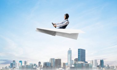 Havacı şapkalı işadamı kağıt düzlemde oturuyor ve direksiyonu tutuyor. Pilot yüksek gökdelenler ve ofis binaları ile iş merkezi üzerinde kağıt uçak sürüş. Bulutlu mavi gökyüzü arka plan
