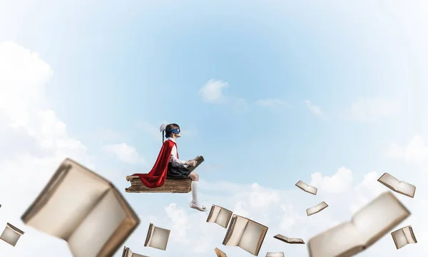 戴面具 披着斗篷的小孩在书本上飘浮 在天空中看书 — 图库照片