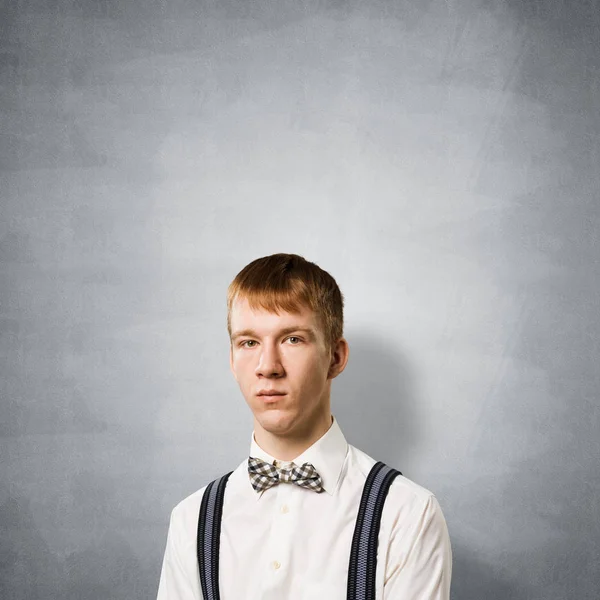 面容严肃沉着的男孩 白人红头发学生有自信的面部表情 灰色墙壁背景下穿着白衬衫 领结和吊带衫的时髦男人的画像 — 图库照片