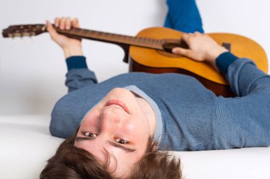 Mutlu genç adam gitarla kanepede uzanıyor. Gülümseyen gitarist beyaz koltukta dinleniyor. Yakın plan beyaz müzisyen akustik gitar çalıyor. Müzik aletleri konsepti çalmak.