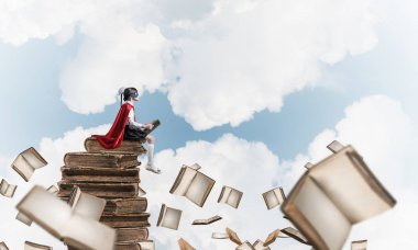 Küçük çocuk maskesi ve cape sittting yığın üzerinde eski gökyüzü ve okuma kitapları