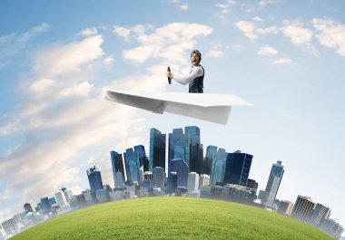 İş merkezinin üzerinde etkileyici havacı sürüş kağıt uçak. Deri kasklı pilot kağıt düzlemde oturuyor ve direksiyonu tutuyor. Yüksek gökdelenler ve binalar ile şehir silueti yuvarlak.